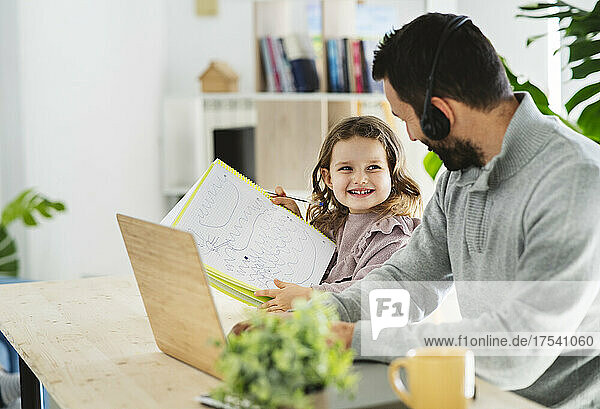 Smiling girl showing drawing to father working at home
