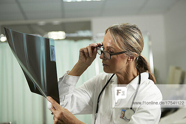 Female doctor holding eyeglasses examining X-ray in medical room
