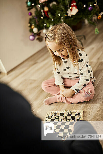 Cute girl playing chess with grandfather at home