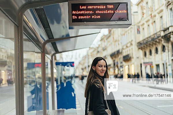 Smiling young woman waiting at tram station in city
