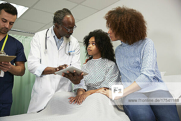 Patientin und Mutter hören dem Arzt zu  der im Krankenhaus einen Tablet-PC hält