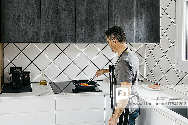 Man preparing fish in cooking pan on stove top at home