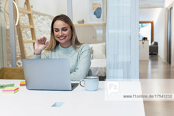 Businesswoman waving on video call at laptop in studio