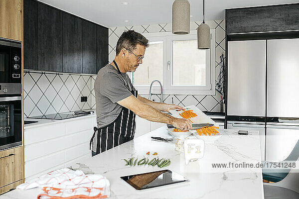 Man putting chopped carrots in bowl preparing food at home