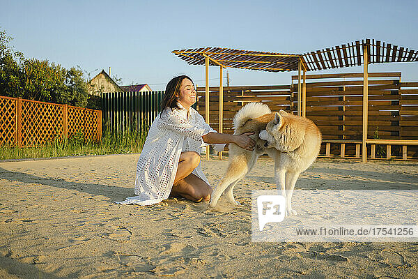 Lächelnde Frau spielt mit Akita-Hund auf Sand