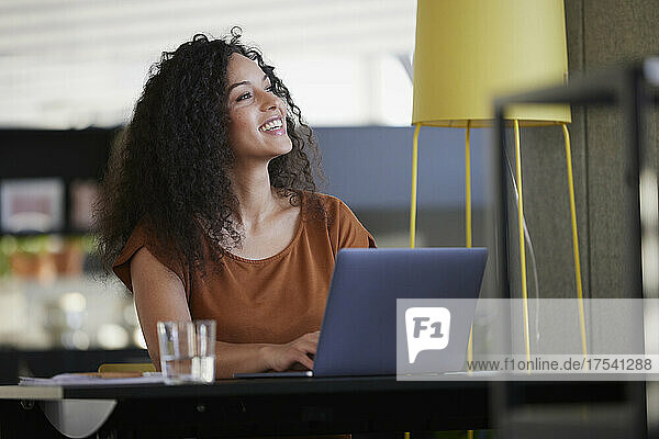Happy businesswoman with laptop on desk day dreaming at workplace
