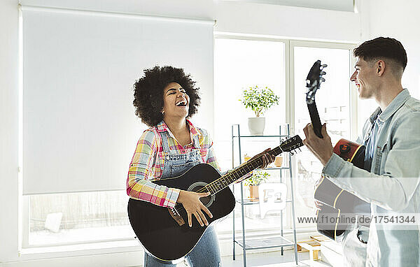 Cheerful young couple playing guitar together at home