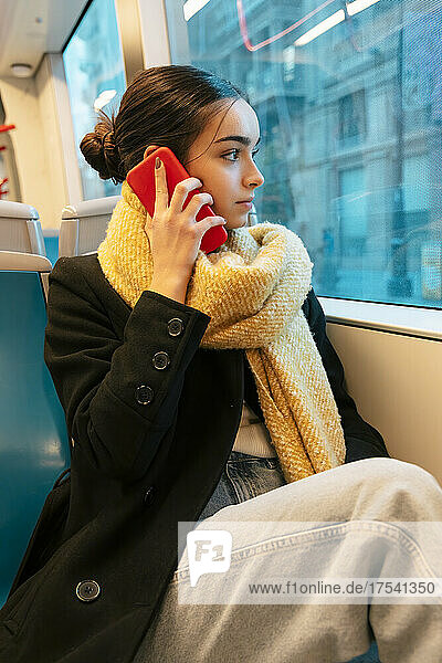 Teenager looking through window and talking on mobile phone in bus