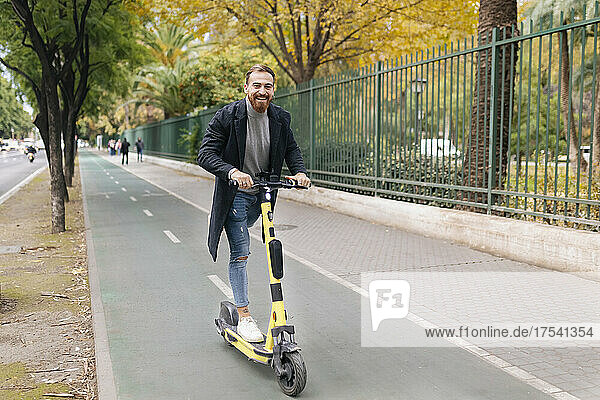 Cheerful man riding e-push scooter on bicycle lane