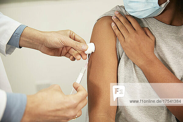 Doctor injecting COVID-19 vaccination to girl through syringe in medical room