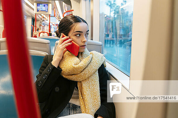Teenage girl looking through window and talking on smart phone in bus