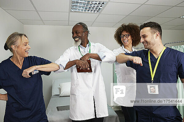 Happy healthcare workers giving elbow bumps in medical room