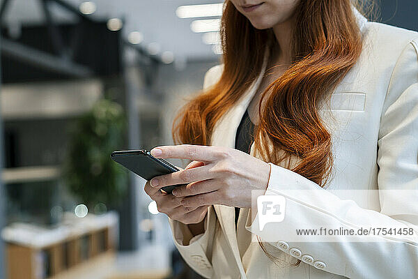 Working redhead woman using mobile phone at office