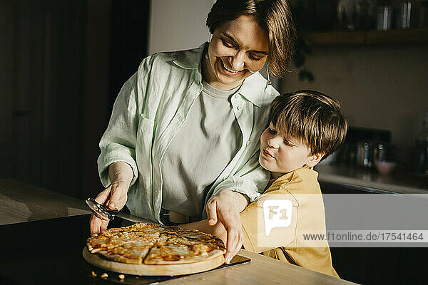 Son embracing mother holding pizza and cutter at home