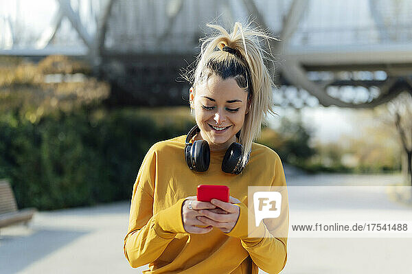 Smiling young woman with wireless headphones using smart phone