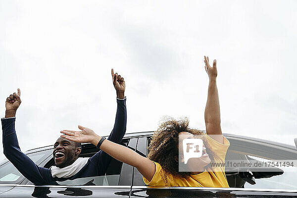 Cheerful friends leaning out of car windows on road trip