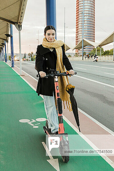 Smiling teenager riding electric push scooter on bicycle lane