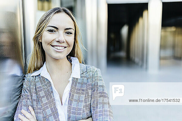 Smiling young blond businesswoman leaning on wall