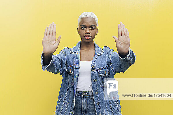 Woman showing stop gesture with both palms against yellow background