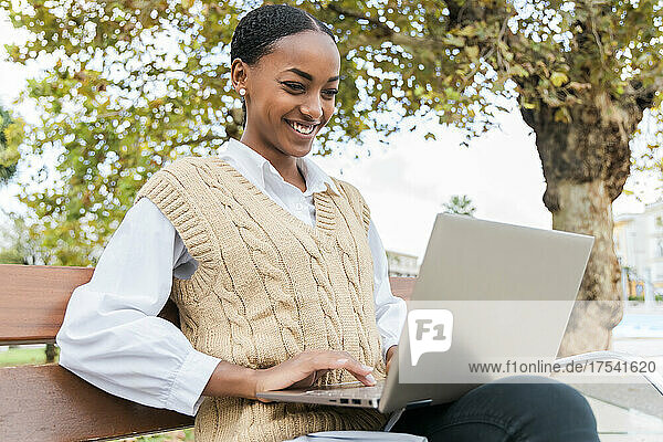 Smiling teenage girl using laptop on bench