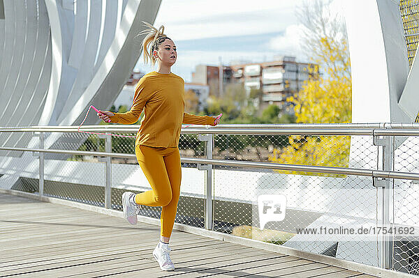 Young woman skipping rope at footbridge on sunny day