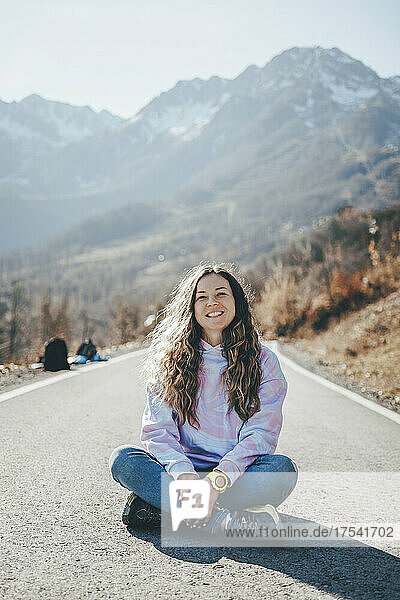 Carefree woman sitting cross-legged on road in front of mountains
