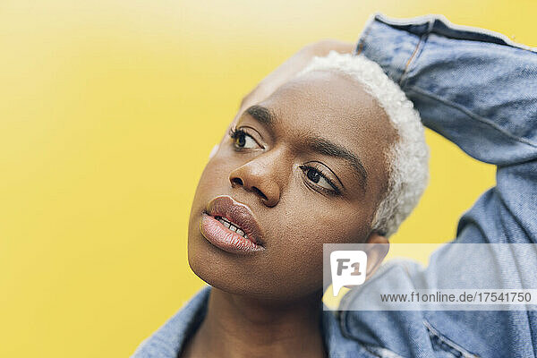 Woman looking away with head in hand against yellow background