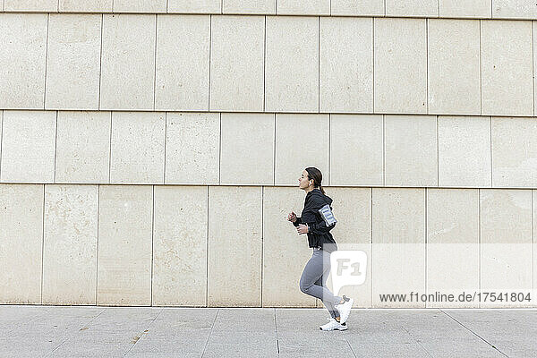 Active woman jogging on footpath by wall