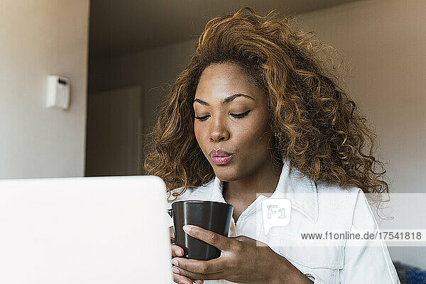 Young woman with laptop having coffee at home