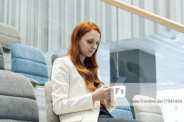 Businesswoman using smart phone sitting on chair in auditorium