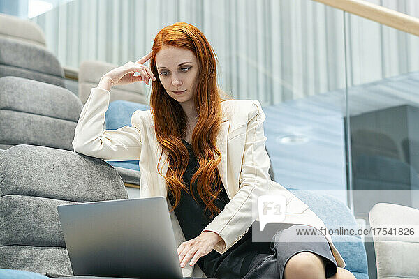 Thoughtful redhead working woman using laptop at auditorium