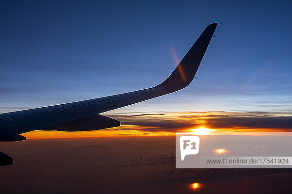 Wing of airplane flying against setting sun