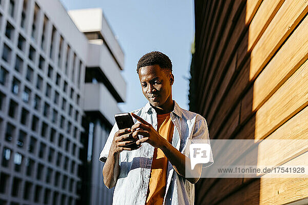 Mann benutzt Smartphone an orangefarbener Wand in der Stadt