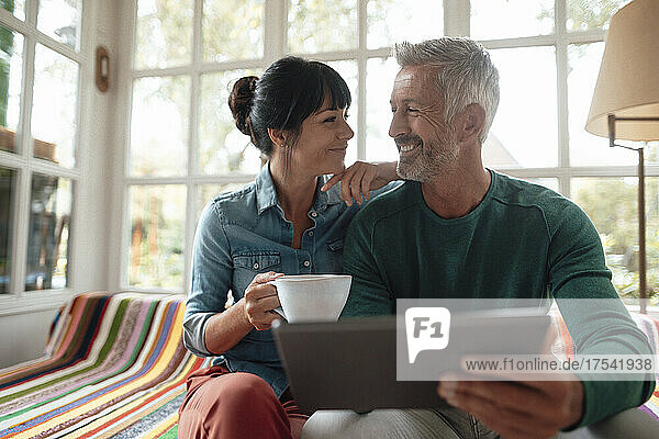Lächelnder Mann mit Tablet-PC neben Frau mit Kaffeetasse auf dem Sofa