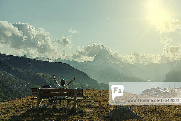Boy with arms outstretched sitting on bench looking at Matterhorn  Zermatt  Switzerland