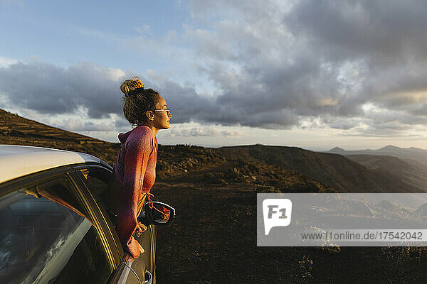 Young woman leaning out of car window looking at mountain landscape