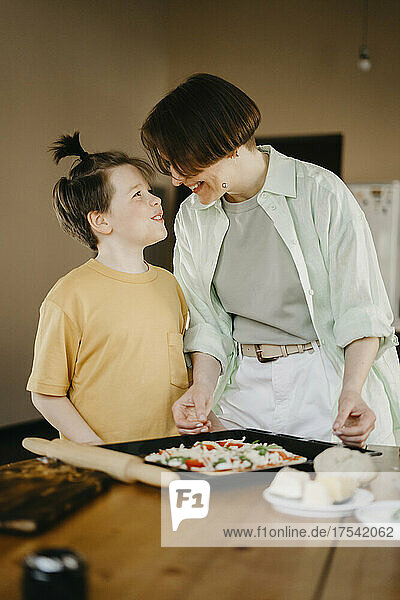 Lächelnder Sohn schaut der Mutter zu  wie sie auf dem Tisch Pizza zubereitet