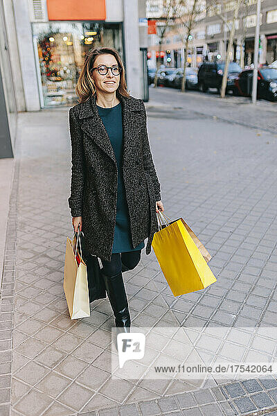 Woman walking on sidewalk holding shopping bags