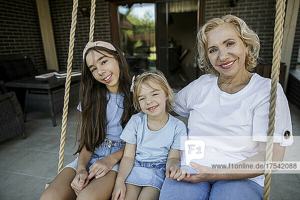 Smiling grandmother with granddaughters sitting on rope swing