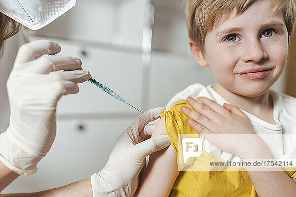 Nurse with protective glove and mask vaccinating boy at center