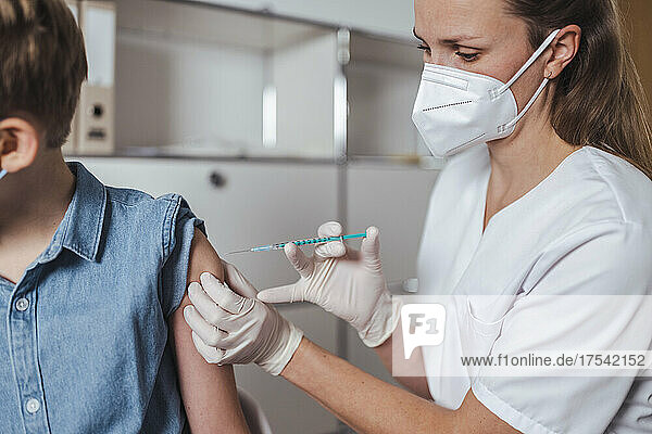 Healthcare worker in face mask administering boy with COVID-19 vaccine