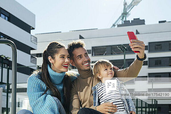 Happy family taking selfie on smart phone in front of building
