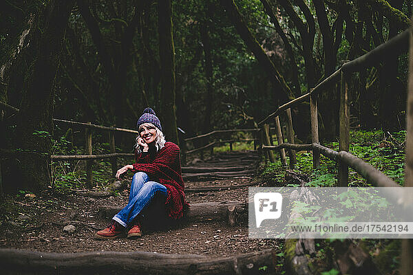 Lächelnde Frau sitzt auf Holzweg im Wald