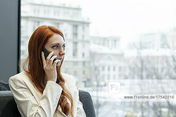 Businesswoman talking on mobile phone by window at office