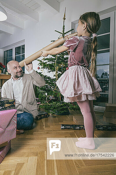 Father looking at daughter through rolled up wrapping paper at home