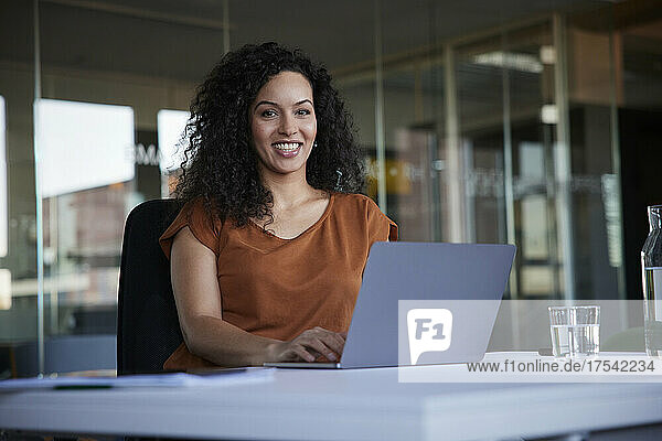 Happy businesswoman with laptop on desk at workplace
