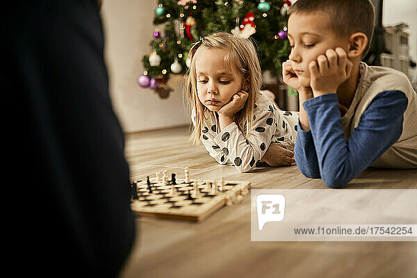 Boy and girl lying on floor looking at chess board at home