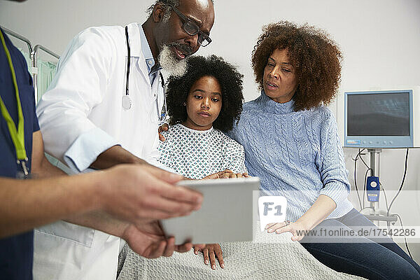 Arzt bespricht die Behandlung am Tablet-PC mit Patientin und Mutter im Krankenhaus