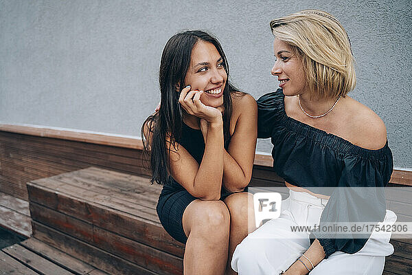 Woman with arm around friend sitting on bench in front of wall
