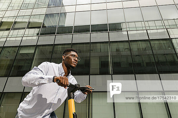 Young man riding electric push scooter by glass building